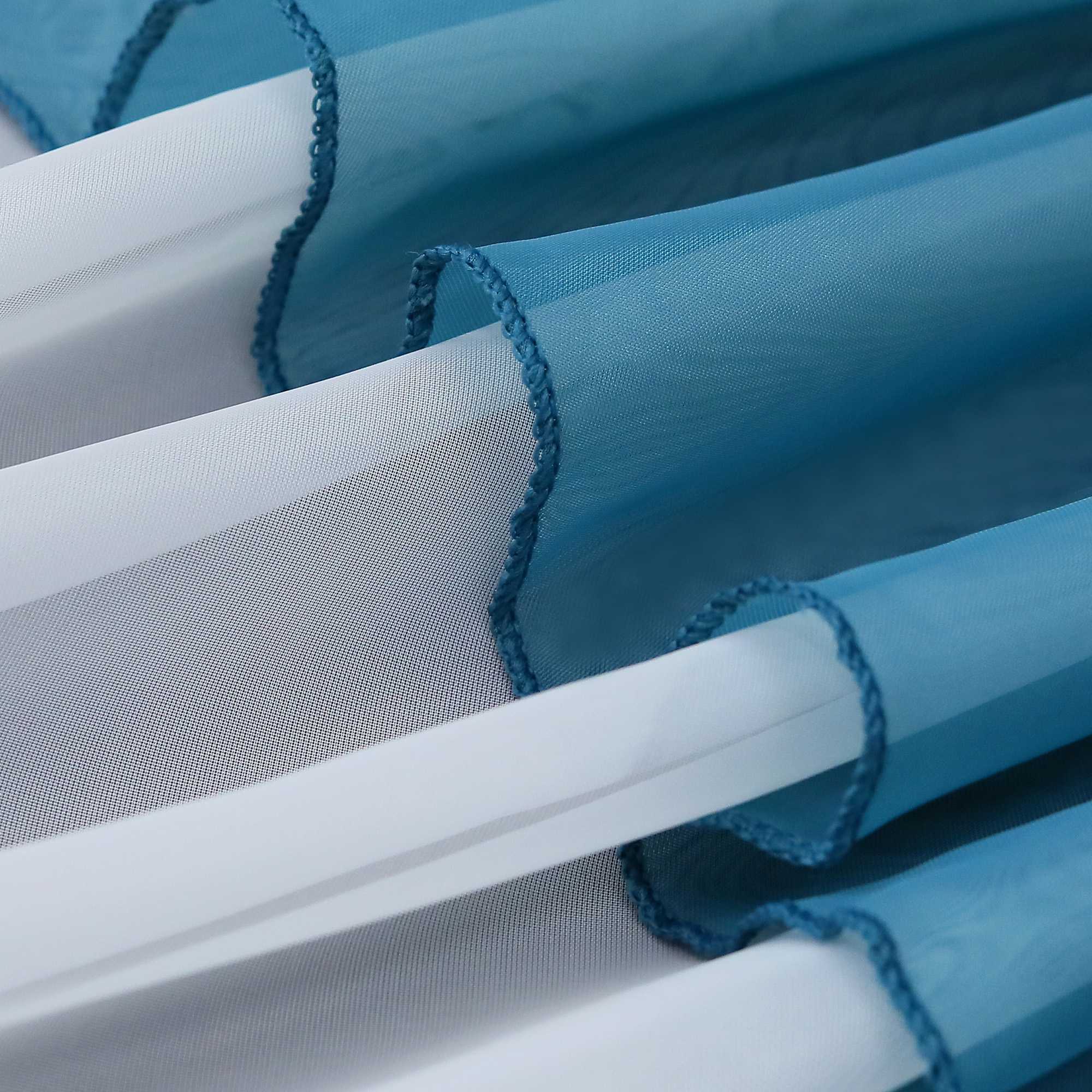 Nahaufnahme mehrerer Lagen eines blauen, halbtransparenten Gardinenstoffs. Die Falten erzeugen ein weiches, welliges Aussehen und reflektieren das Licht.