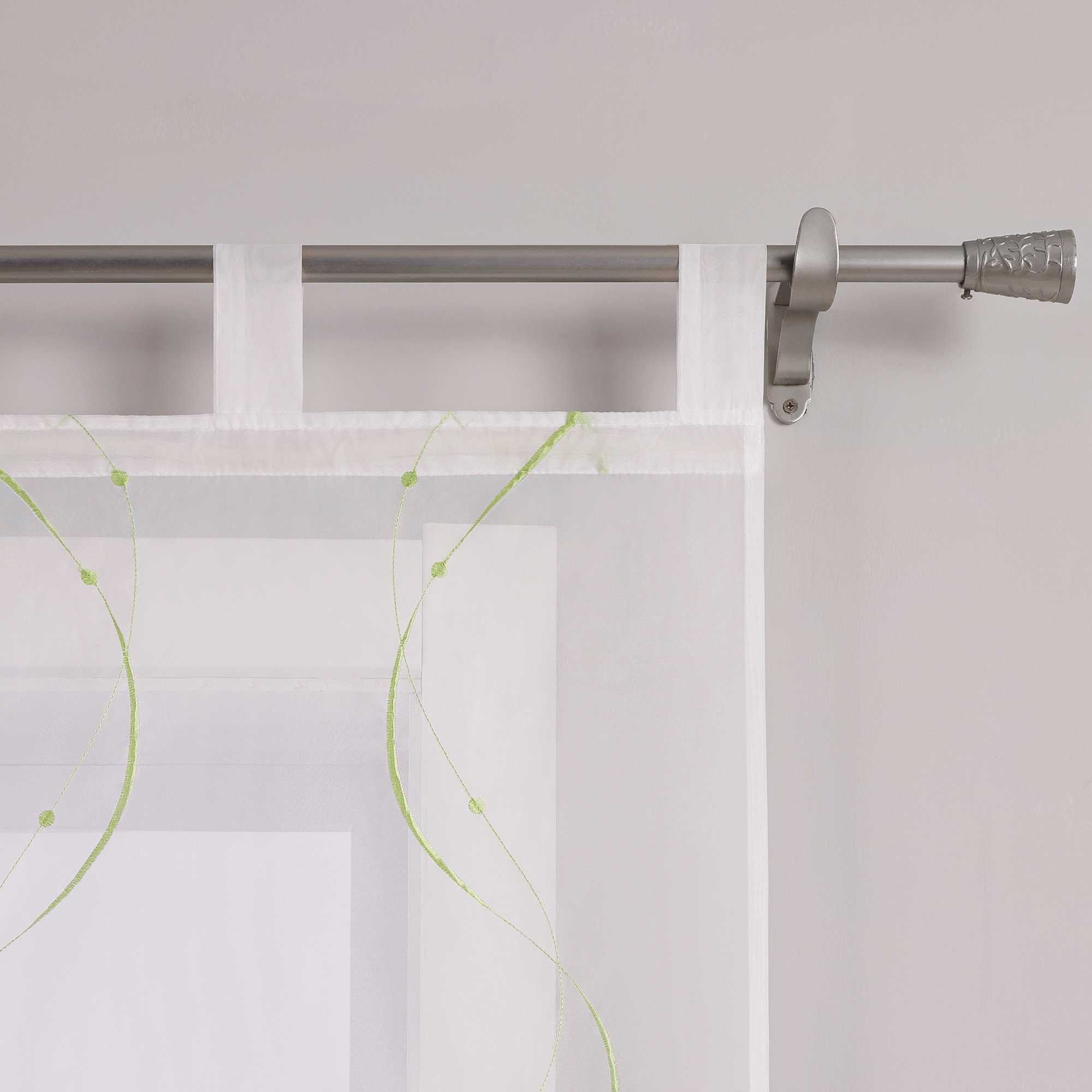 Das Bild zeigt die Details der Gardinenschlaufen. Die Gardine ist mit feinen grünen Naehten in Wellenform und kleinen Punkten am Ende verziert. Sie haengt mithilfe gleichmaessiger weisser Schlaufen an einer Metallstange. Die Verarbeitung an den Naehten ist sauber, das Material wirkt hochwertig.