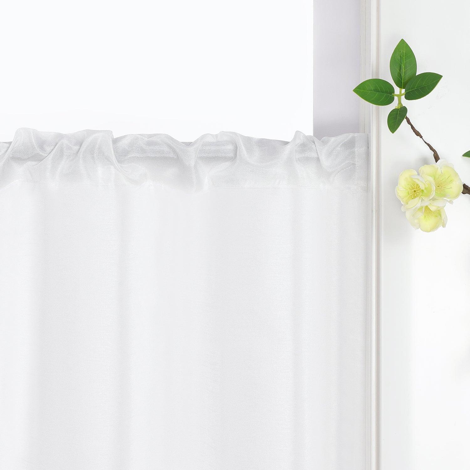 Die weiße Scheibengardine hängt elegant am Vorhangstab. Der Stoff fällt natürlich und gerade, während Blumen als Dekoration daneben platziert sind.
