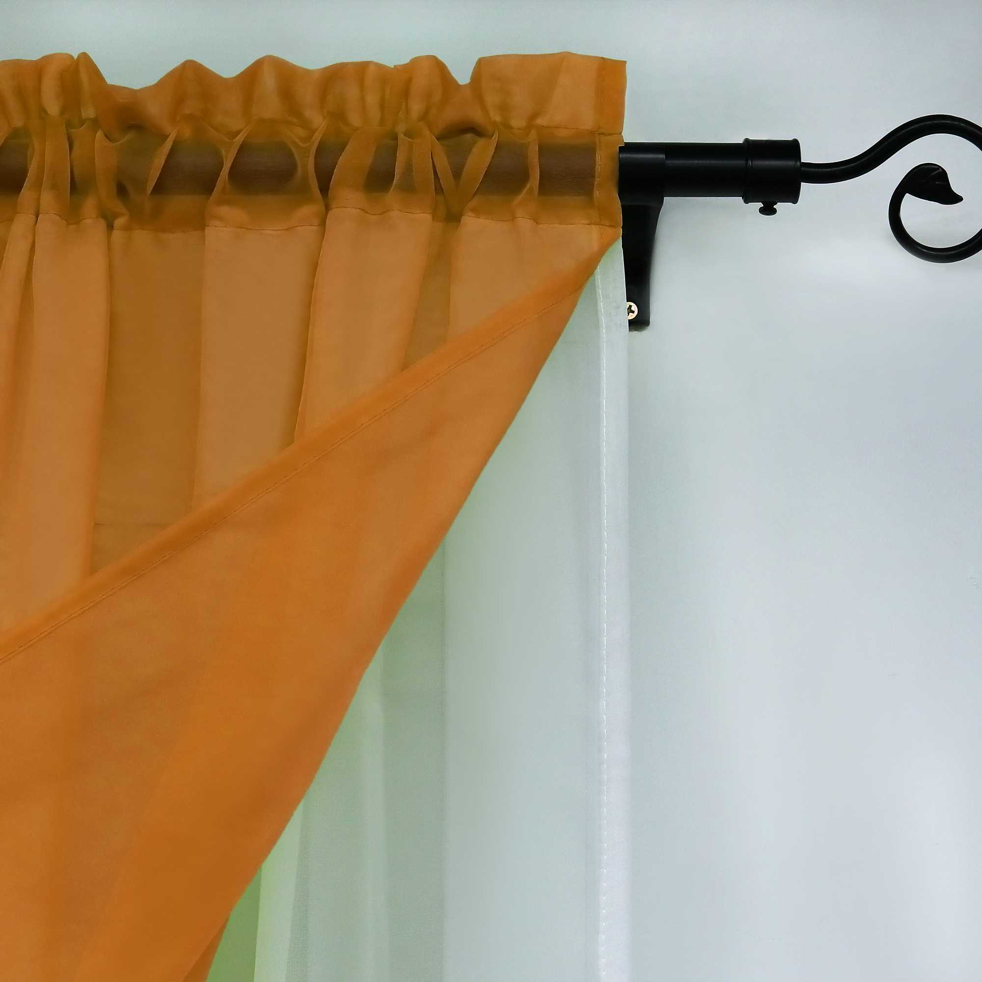 Nahaufnahme der orangefarbenen halbtransparenten Gardinen. Der Saum des oberen Teils der Gardinen sorgt für eine gleichmäßige Faltung, während die Gardinen an einer eleganten schwarzen Gardinenstange befestigt sind.