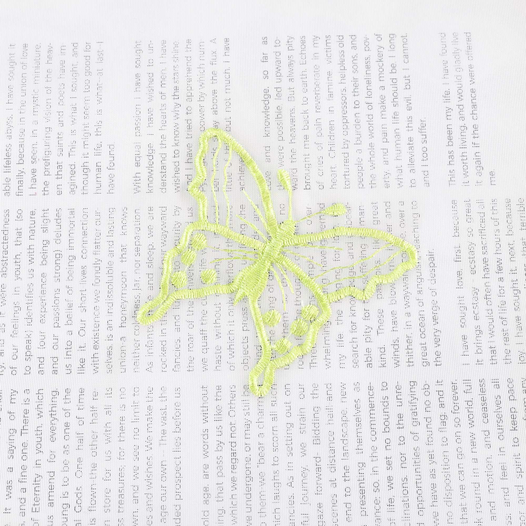 Nahaufnahme einer grünen Schmetterlingsstickerei, die auf einem transparenten weißen Stoff flach ausgebreitet liegt. Die grünen Schmetterlinge sind sorgfältig in das Gewebe eingearbeitet.