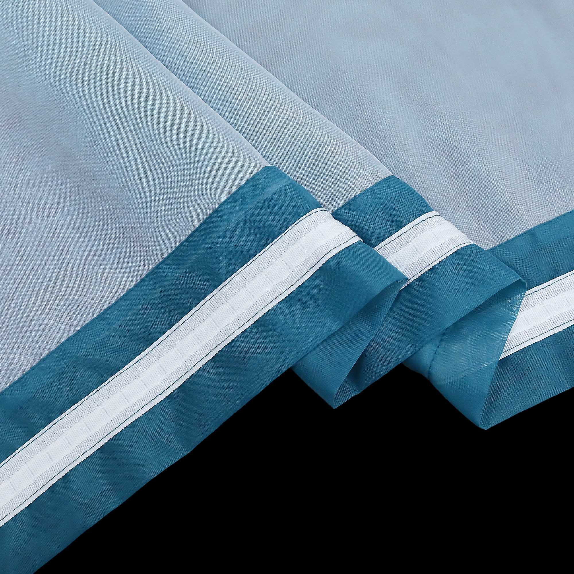 Detail eines blauen halbtransparenten Gardinenstoffs mit deutlich sichtbarem Saum und sauber gefalteten Kanten. der blaue Stoff hat weiße Nähte.