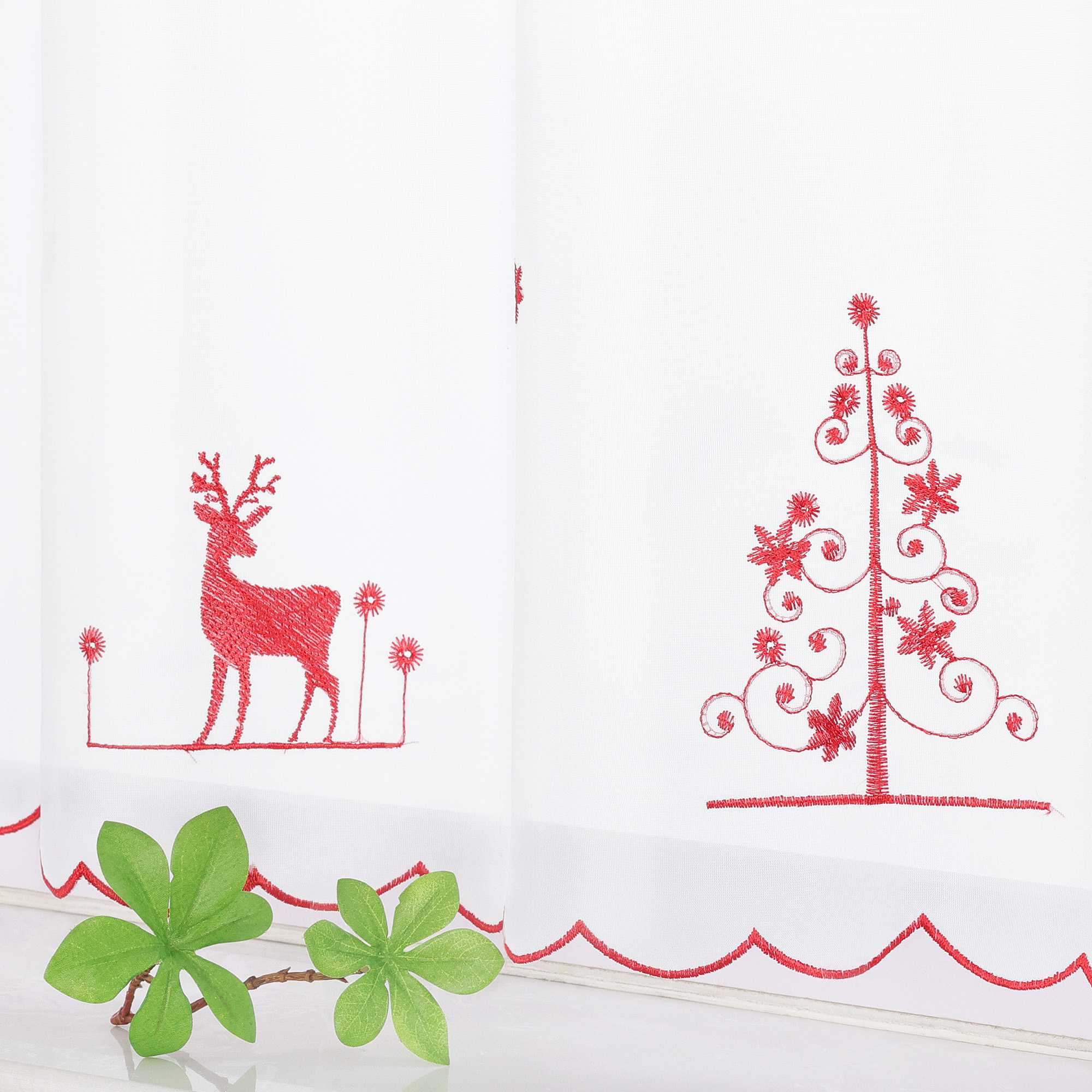 Die rote Rentier- und Weihnachtsbaum-Stickerei ist mit feinen, gleichmäßigen Stichen gefertigt, die das festliche Design lebendig und detailliert wirken lassen. Die Gardine hängt elegant am Fenster und verleiht dem Raum sofort eine weihnachtliche Atmosphäre.