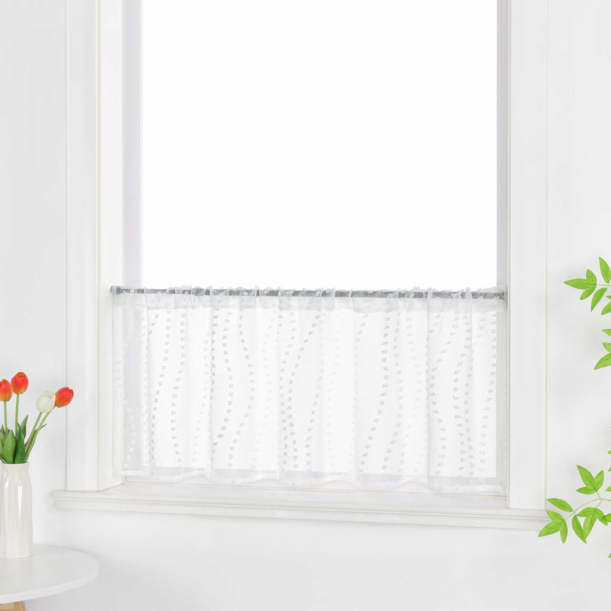 In der Seitenansicht ist die weiße, transparente Scheibengardine mit ihrem 3D-Punktemuster deutlich sichtbar. Die Gardine lässt das Licht sanft durch und schafft eine helle, luftige Atmosphäre im Raum. Die grünen Pflanzen am Fenster ergänzen das natürliche Ambiente perfekt.