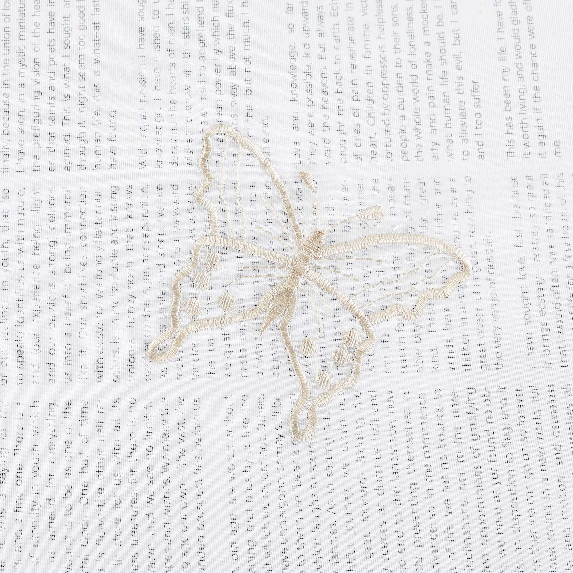 Nahaufnahme einer beigen Schmetterlingsstickerei, die auf einem transparenten weißen Stoff flach ausgebreitet liegt. Die beigen Schmetterlinge sind sorgfältig in das Gewebe eingearbeitet.