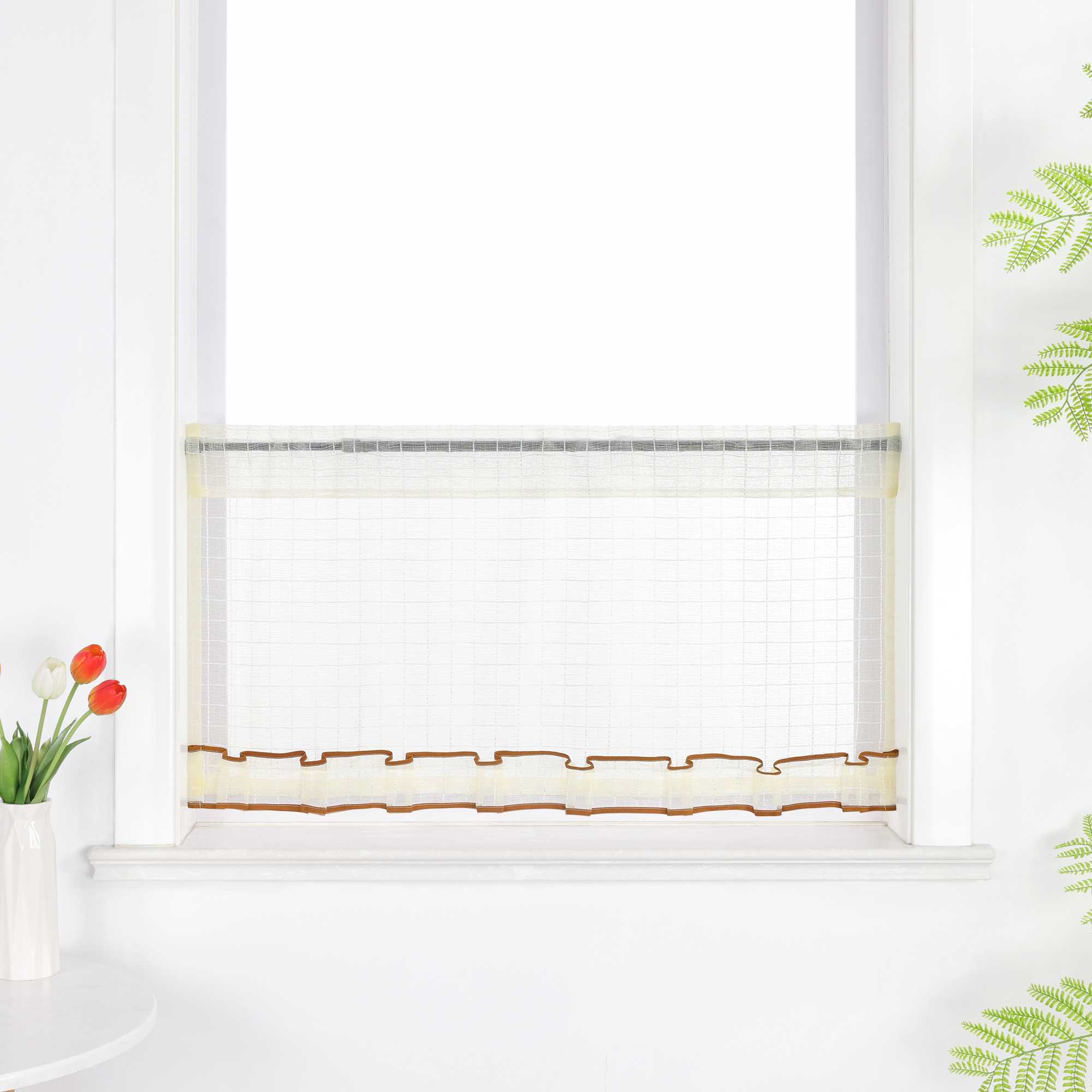 Gelber, transparenter Kurzvorhang hängt vor dem Fenster. Die Oberfläche zeigt ein feines Karomuster, unten verläuft ein dekoratives Band in Braun. Der obere Rand ist gerafft und bildet leichte Falten.