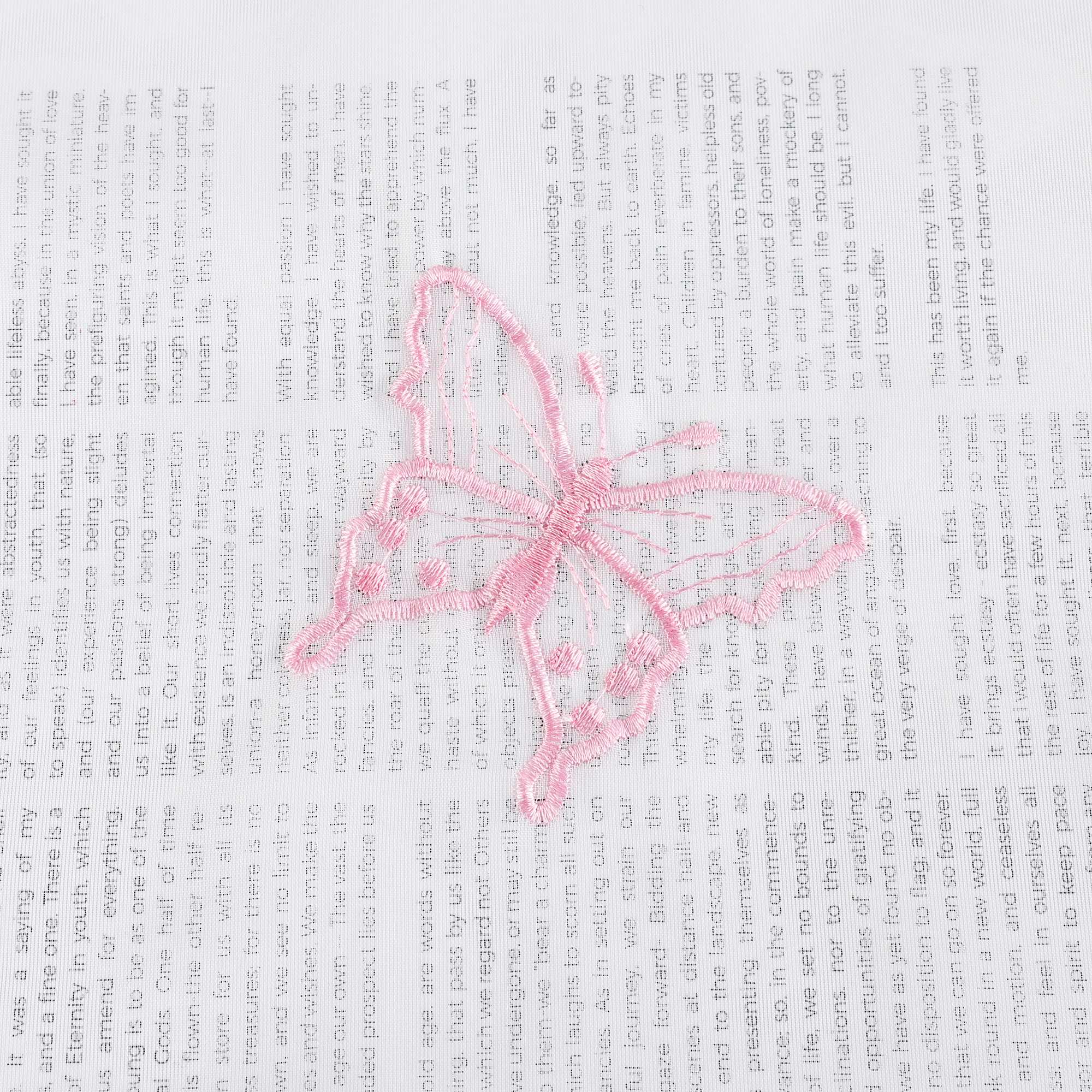 Nahaufnahme einer rosa Schmetterlingsstickerei, die auf einem transparenten weißen Stoff flach ausgebreitet liegt. Die rosa Schmetterlinge sind sorgfältig in das Gewebe eingearbeitet.