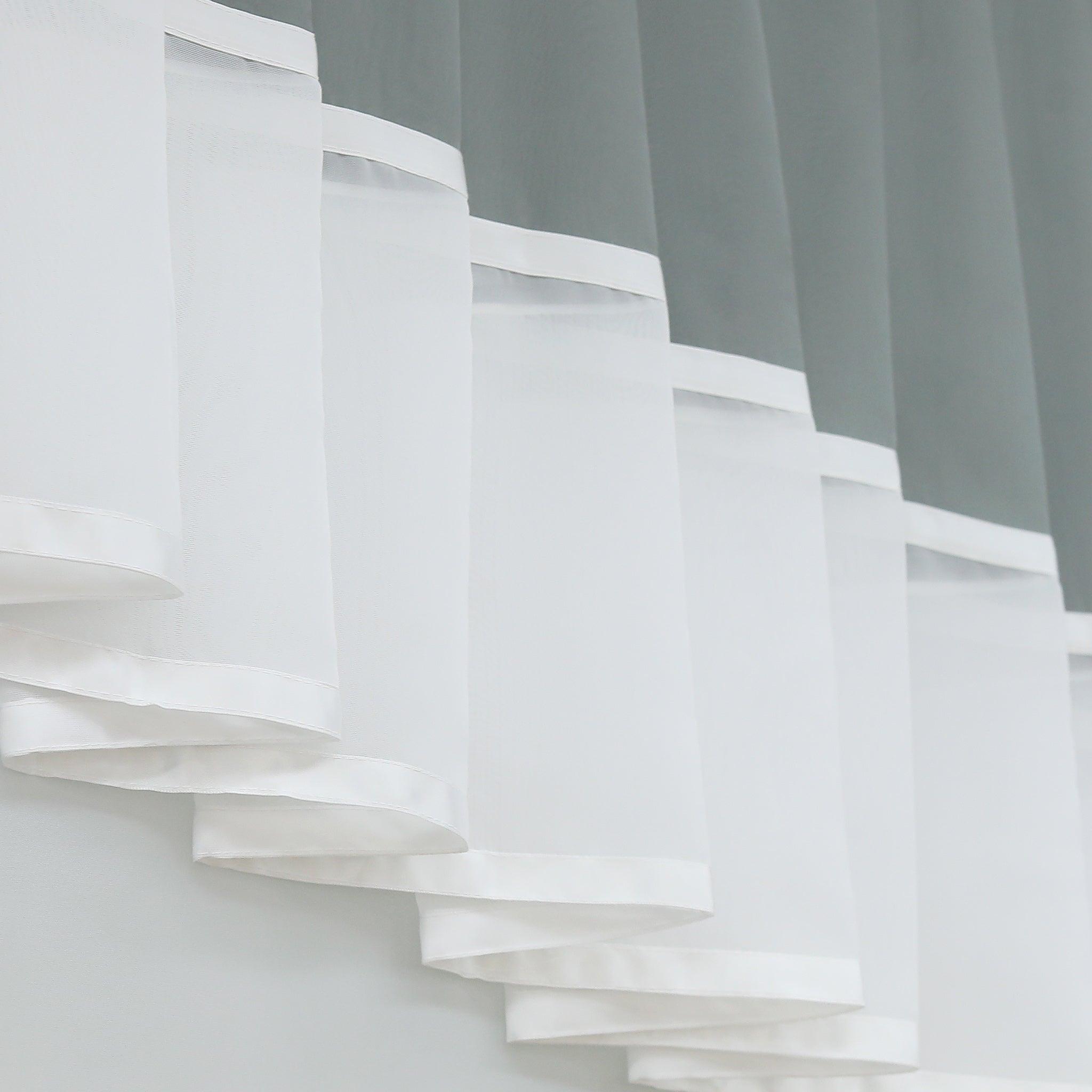 Dies ist ein Detailbild des weißen, transparenten Teils des Vorhangs. Der Stoff ist leicht und weist eine saubere Kantenborte auf. Die Falten sind schichtweise angeordnet, was dem Vorhang eine schöne, dekorative Struktur und eine harmonische Tiefe verleiht.