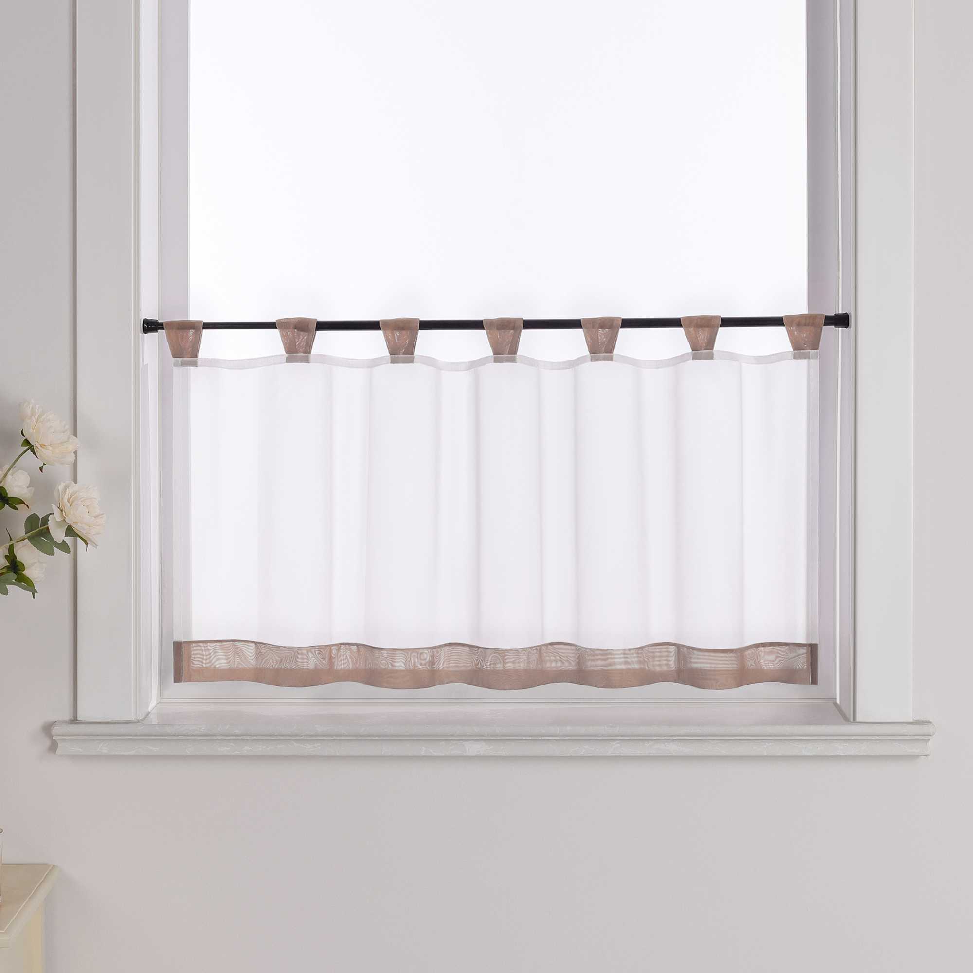 Die braune Scheibengardine hängt vor einem Fenster, wobei die Hintergrundwand weiß ist. Der Vorhang ist transparent und wird von blumigen Dekorationen an der Seite begleitet.