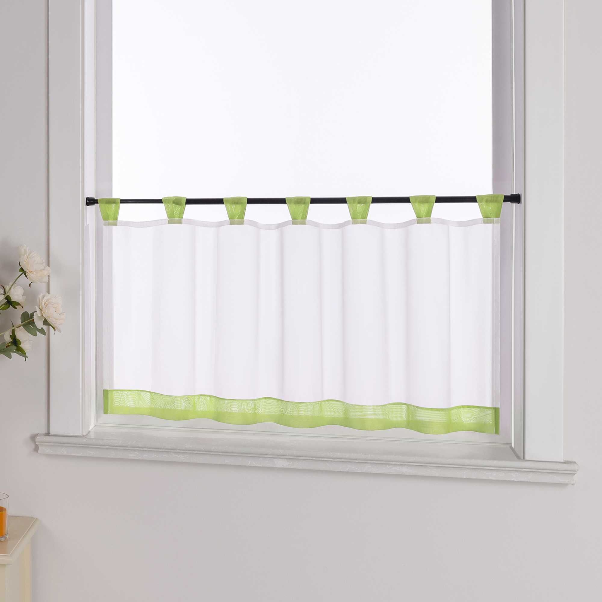 Der weiße Vorhang mit gruene Dekorband wird aus einem seitlichen Winkel fotografiert. Die weiße Wand im Hintergrund betont die Schlichtheit des Designs, während blumige Dekorationen an der Seite dem Raum eine zarte, natürliche Atmosphäre verleihen.