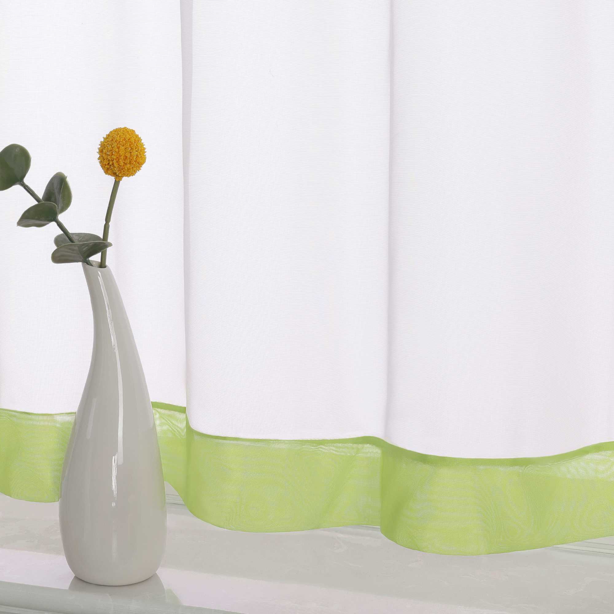 Die Unterkante des Vorhangs wird im Detail gezeigt, mit einem gruene Dekorband als stilvollem Akzent. Ein Vase im Vordergrund ergänzt die Szene und fügt dem Raum eine harmonische, dekorative Note hinzu, die den eleganten Look des Vorhangs unterstreicht.