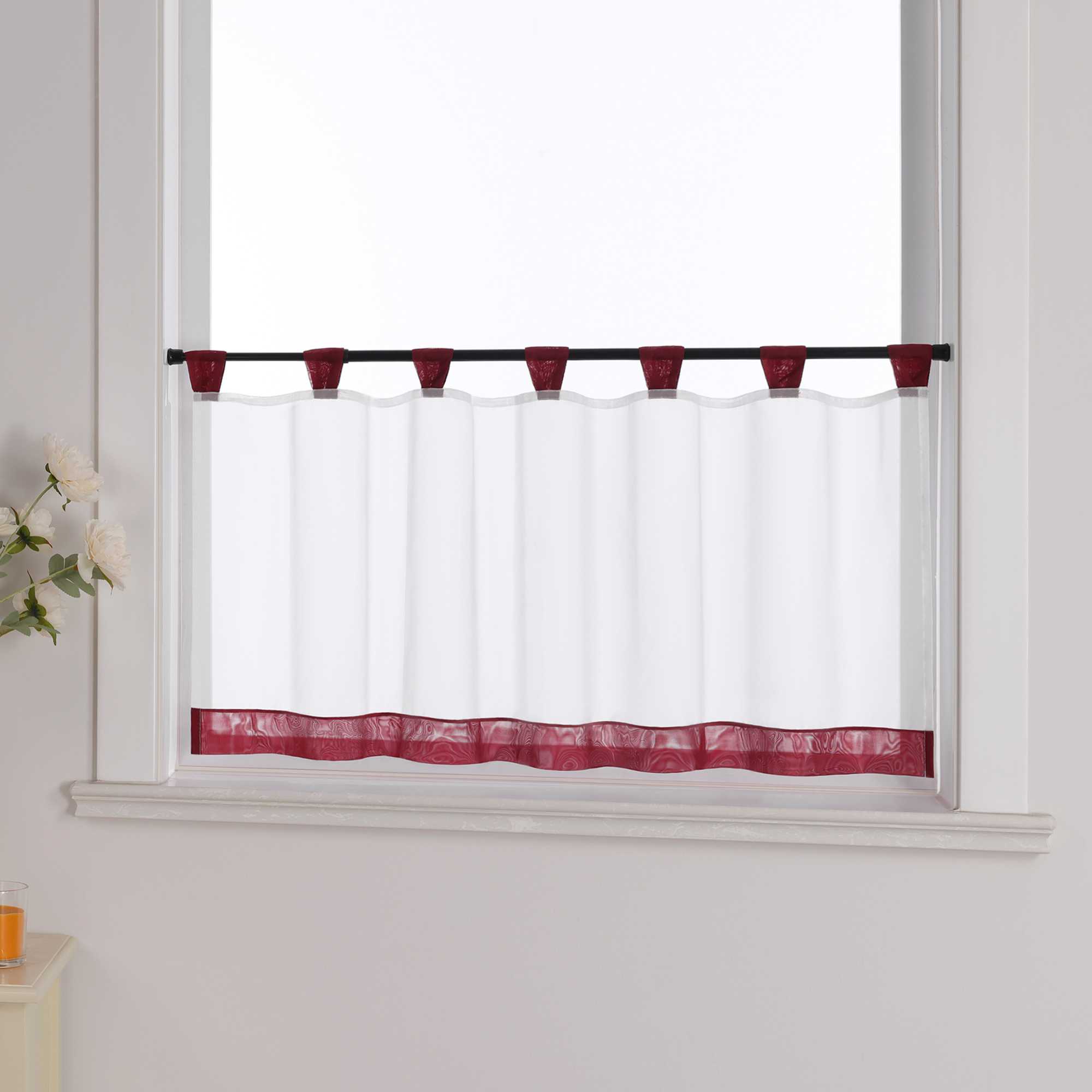 Die weinrot Scheibengardine hängt vor einem Fenster, während die weiße Hintergrundwand im Hintergrund sichtbar bleibt. Der transparente Vorhang lässt das Licht durch, während er von blumigen Dekorationen an der Seite sanft ergänzt wird, was dem Raum eine leichte und frische Atmosphäre verleiht.