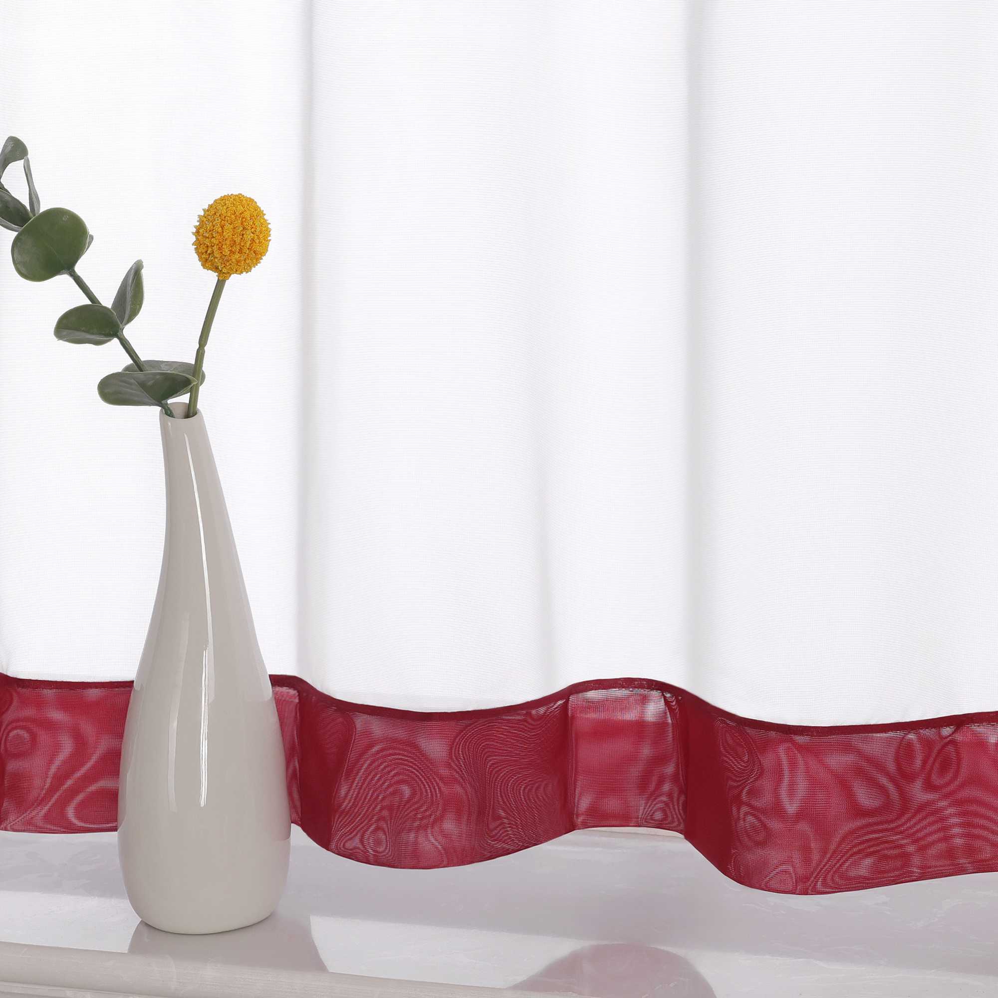 Die Unterkante des Vorhangs wird im Detail gezeigt, mit einem weinrot Dekorband als stilvollem Akzent. Ein Vase im Vordergrund ergänzt die Szene und fügt dem Raum eine harmonische, dekorative Note hinzu, die den eleganten Look des Vorhangs unterstreicht.