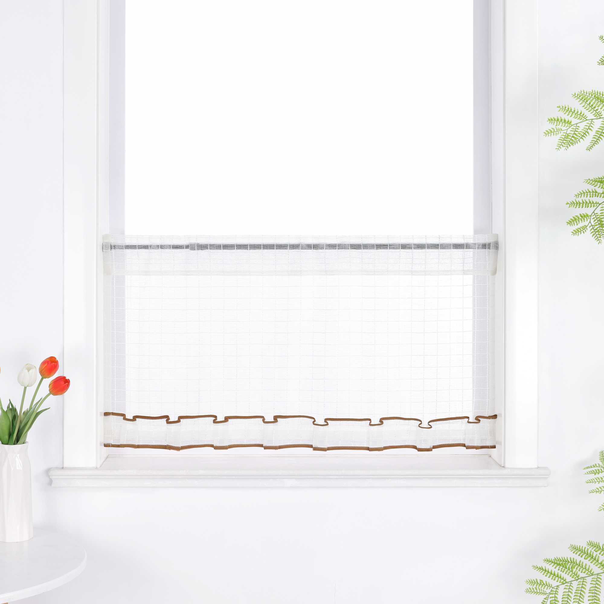 Weißer, transparenter Kurzvorhang hängt vor dem Fenster. Die Oberfläche zeigt ein feines Karomuster, unten verläuft ein dekoratives Band in Braun. Der obere Rand ist gerafft und bildet leichte Falten.