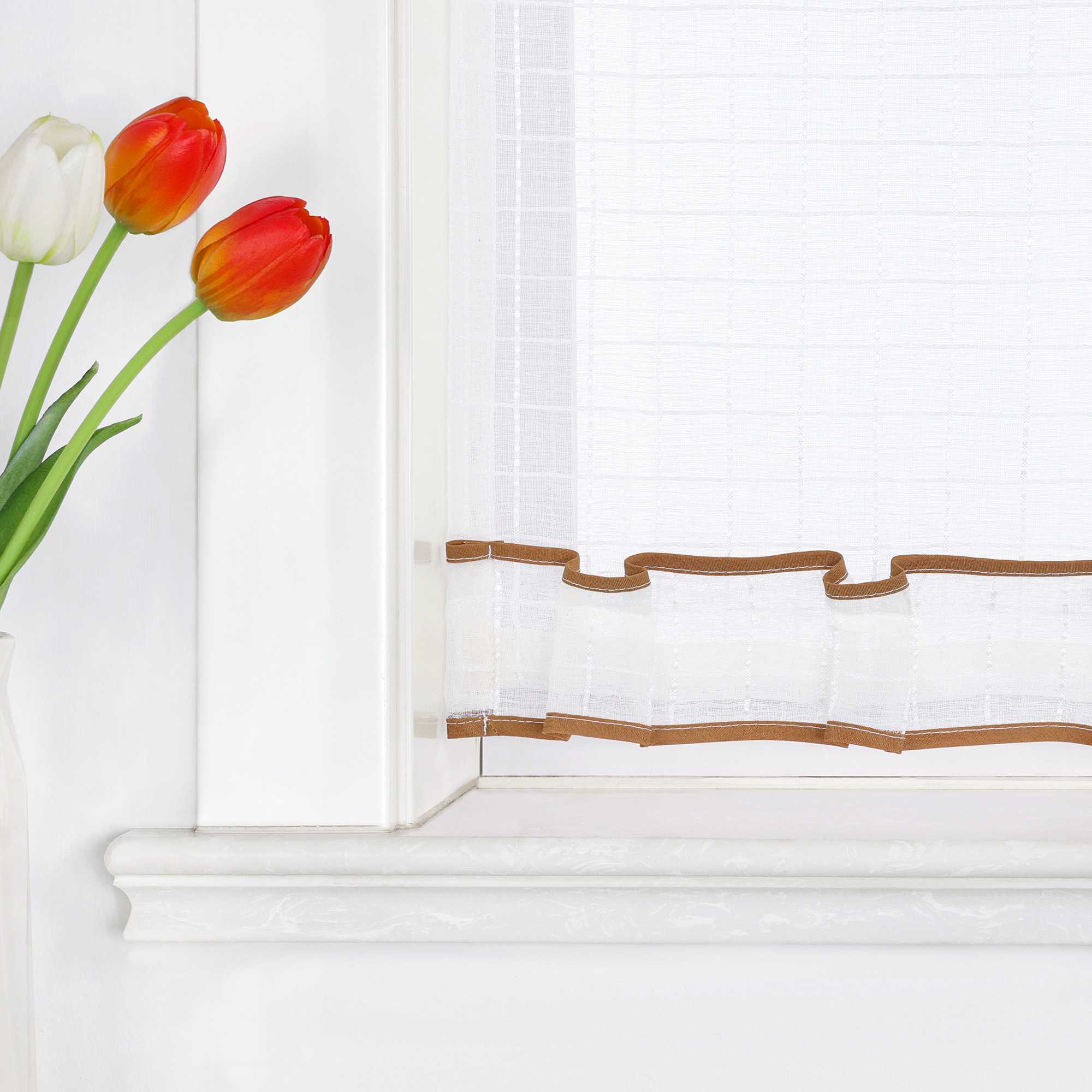 Nahaufnahme der unteren Fensterhälfte mit weißem, transparentem Kurzvorhang. Der untere Rand ist mit einer gewellten, braunen Borte verziert. Links im Bild stehen rote, orangefarbene und weiße Tulpen in einer Vase.